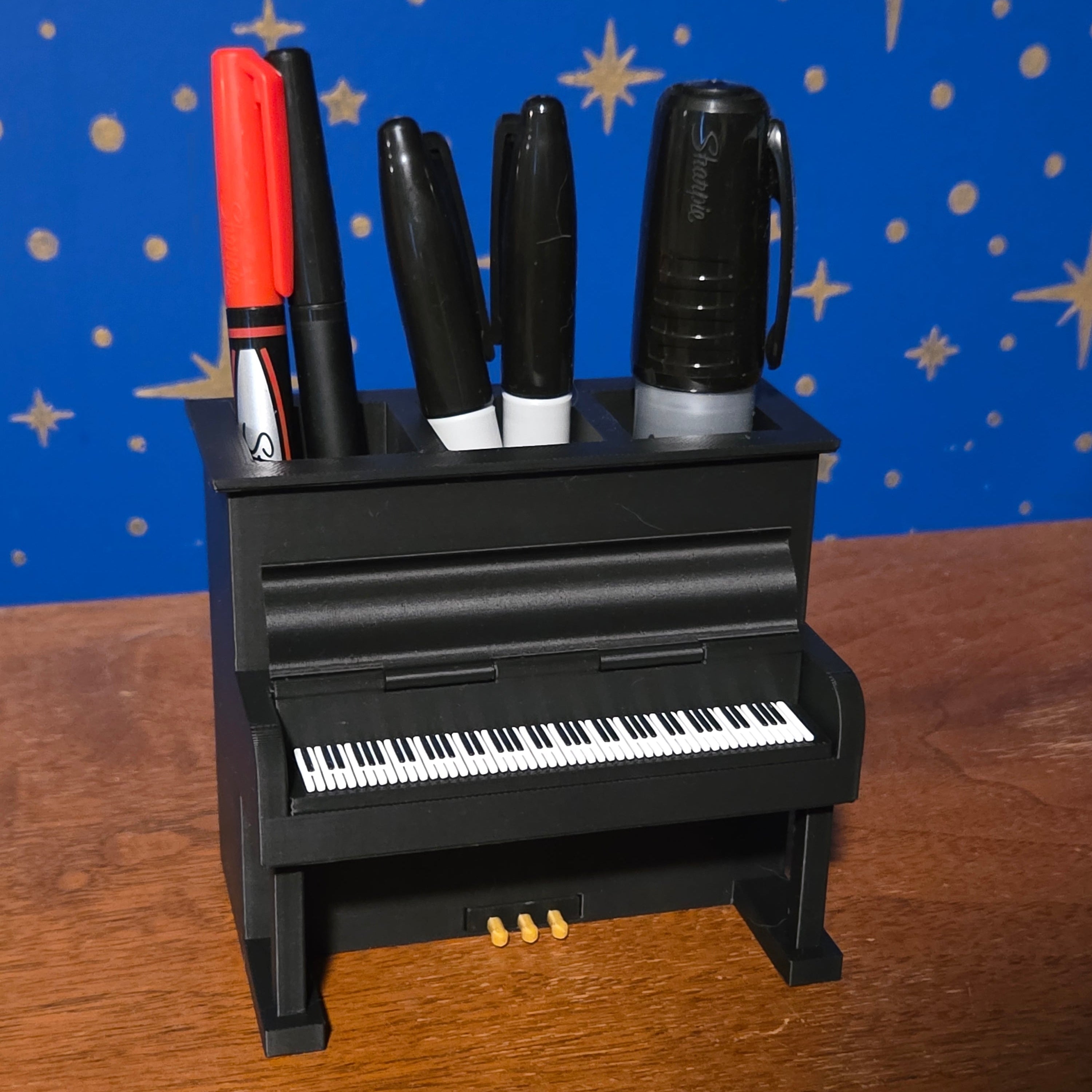 Keyboard-style holder with markers in front of a blue surface with star patterns